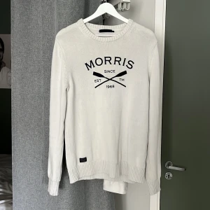 Vit tröja från Morris - Säljer en stilren vit tröja från Morris med svart tryck på framsidan. Tröjan har långa ärmar och ribbade muddar vid ärmslut och nederkant. Priset kan diskuteras.