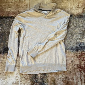 Beige tröja med dragkedja från Jack & Jones - Säljer en stilren beige tröja från Jack & Jones med dragkedja vid halsen. Tröjan har långa ärmar och ribbade muddar vid ärmslut och nederkant. Perfekt för en avslappnad look. Storlek S/Xs