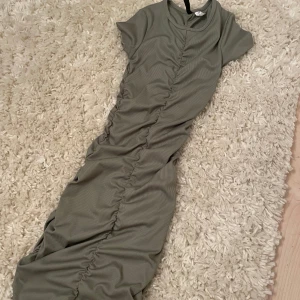Grön ribbad klänning från H&M divided - Snygg grön ribbad klänning från H&M Divided med korta ärmar och en åtsittande passform. Klänningen har en rynkad detalj längs framsidan, sidorna och i bak som ger en cool look. Är väldigt tight och ganska liten i storleken. Ganska använd men inga märken på det. Kan sänka pris