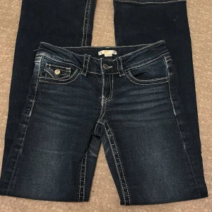 Mörkblå jeans från Gina Tricot - Snygga mörkblå jeans från Gina Tricot med kontrasterande sömmar och klassisk femficksdesign. Jeansen har en knapp och dragkedja framtill samt dekorativa bakfickor med knappar. Perfekta för en avslappnad stil.