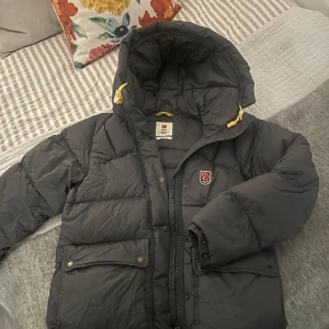 Grå/grön dunjacka från Fjällräven - Säljer en grå (kan se mörkgrön ut i vissa ljus) från Fjällräven Expedition Down Jacket med huva och gula dragskor. Det är storlek S men skulle absolut passa en XS eller M också. Jackan är använd flitigt i två vintrar, så det kan finnas några sminkfläckar vid kragen men inget man tydligt ser. Köpte för 7000 kr! 