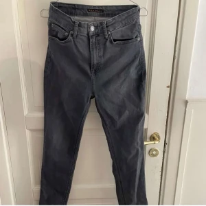 Mörkgrå jeans från Nudie Jeans - Snygga mörkgrå jeans från Nudie Jeans med klassisk femficksdesign och svarta detaljer på bakfickan. Jeansen har en rak passform och är tillverkade i mjukt bomullsjeansmaterial. Perfekta för dig som gillar stilrena och tidlösa byxor. Nypris: 1200kr