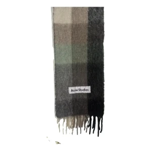 Rutig halsduk från Acne Studios - Supermjuk och fluffig halsduk från Acne Studios i rutigt mönster med toner av grått, grönt och brunt. Stora rutor och långa fransar i ändarna ger en cool vibe. Perfekt accessoar för att lyfta din höst- eller vinterstil.