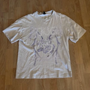 Vit oversized t-shirt Black Squad XS - Vit oversized t-shirt från Black Squad i storlek XS. Tryck framtill med motiv av en rytande varg och grafisk text i lila toner. Klassisk rund hals och korta ärmar. Skön och avslappnad passform. 