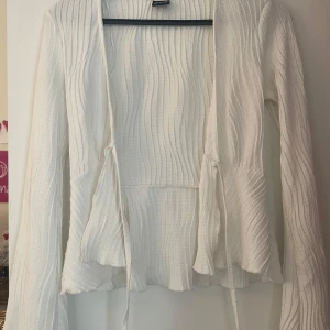 Vit ribbad kofta med knytband - Superfin vit kofta från Bik Bok med ribbad struktur och långa ärmar. Den har snygga knytband framtill och en lätt vågig kant nedtill. Perfekt att slänga över en topp för en chill och stilren look.