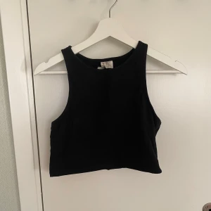 Svart top - Enkel och stilren svart  topp från . Toppen har hög halsringning och är ärmlös med breda axelband. Perfekt att matcha med jeans eller kjol för en clean look.