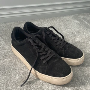 Svarta mockasneakers från Vagabond - (STORLEK 46)Svarta sneakers från Vagabond i mocka med klassisk låg profil och vita platta sulor. Skorna har rund tå, svarta snören och stilren design som passar till det mesta. Perfekta för dig som gillar en clean och enkel look.