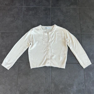 Beige kofta från Zara med knappar - Snygg beige kofta från Zara i storlek S. Den har rund halsringning, ribbade muddar och knäppning framtill med matchande knappar. Mjuk och stickad känsla. Liten i storlek och mer som en xs/xxs.
