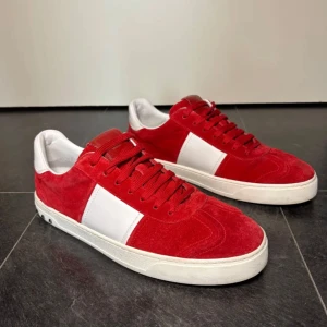 Valentino Flycrews - Snygga röda sneakers från Valentino Garavani i mocka med vita detaljer och klassiska nitar på sulan. Skorna har vit platt sula, rund tå och snörning. Perfekta för dig som vill ha en lyxig sko.  Kan tänka mig gå ner i priset vid en snabb affär.