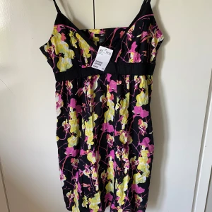 Blommig kortklänning från H&M - Superfin kortklänning från H&M med svart botten och färgglada blommor i rosa och gult. Klänningen har smala axelband, v-ringning och markerad midja. Perfekt för varma dagar när du vill sticka ut lite extra.