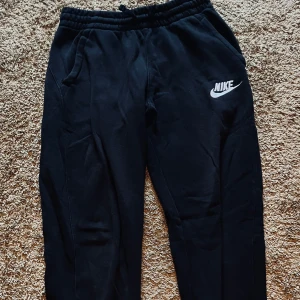 Svarta mjukisbyxor från Nike XL (158-170) - Svarta mjukisbyxor från Nike med broderad vit logga på ena benet. Byxorna har resår i midjan och sidofickor, perfekta för chill eller träning. Tillverkade i mjukt material som känns skönt mot huden. Nypris 429kr! 