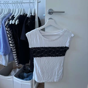Vit topp med svart spetsdetalj - Vit ärmlös topp med bred svart spets över bröstet. Rund halsringning och figurnära passform. Perfekt för dig som gillar kontraster och vill ha en enkel men ändå unik look. Ganska skrynklig på bilden men om man stryker så ser den sprillans ny ut.
