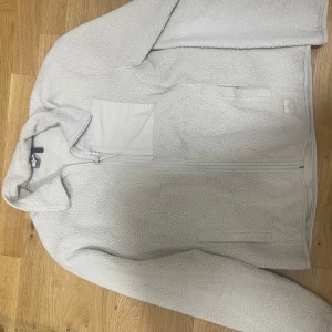 Vit teddyjacka från McKinley M - Säljer en vit teddyjacka från McKinley i storlek medium. Jackan har hel dragkedja, hög krage och en praktisk bröstficka. Mjuk och fluffig fleece som håller dig varm under kyliga dagar. Perfekt för dig som gillar en clean och enkel stil.