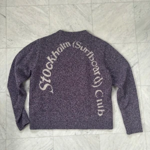 Tröja från Stockholm Surfboard Club - Snygg lila stickad tröja från Stockholm (Surfboard) Club i 100% merinoull. Tröjan har ett coolt tryck på ryggen. Den köptes i vintras på Paul & Friends för 4600 kr och har endast använts ca 10 gånger.