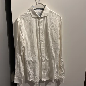 Vit skjorta från Bläck, tailored fit - Klassisk vit skjorta från Bläck med snygg tailored fit. Skjortan har långa ärmar, knappar framtill och en stilren krage. Skjortan är ny tvättad därav skrynklig. Storlek M 39/40
