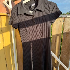 Svart ribbad kortklänning H&M Divided - Svart ribbad kortklänning från H&M Divided med krage och knappar framtill. Klänningen har korta ärmar och en slim passform som framhäver siluetten.