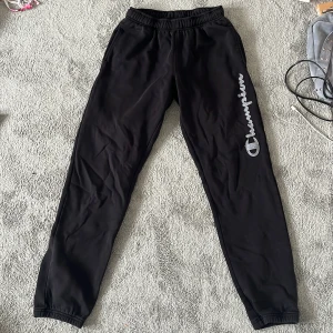 Lågmidjade mjukisbyxor Champion  - Svarta lågmidjade mjukisbyxor från Champion i storlek S. Byxorna har resår i midjan (snören på insidan) och vid bensluten samt ett stort grått Champion-tryck längs ena benet. Perfekta för chill eller träning, riktigt sköna och stilrena.