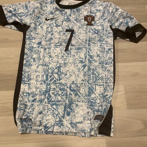  Ronaldo #7 fotbollströja blåvit - Snygg fotbollströja med Ronaldo och nummer 7 på ryggen. Tröjan har ett unikt blått och vitt abstrakt mönster, svarta detaljer på sidorna och är tillverkad i Dri-Fit material som andas. Perfekt för dig som vill sticka ut på planen.