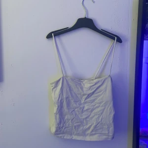 Vit linnetopp från Gina Tricot - Säljer en enkel och stilren vit linnetopp från Gina Tricot i storlek S. Toppen har tunna axelband och rak passform, perfekt att matcha med jeans eller kjol. Materialet känns mjukt och lätt mot huden. En klassiker i garderoben! Den ser ut som en magtröja på!