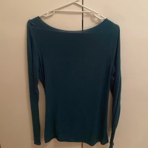 Mörkgrön långärmad tröja - Enkel och stilren mörkgrön långärmad tröja med rund halsringning. Tröjan har en smal passform och är gjord i ett mjukt, tunt material som känns skönt mot huden. Perfekt att matcha med jeans eller kjol för en clean look.