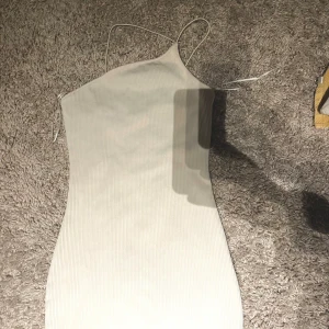 Vit ribbad kortklänning från Divided - Supersnygg vit ribbad kortklänning från Divided med tunna axelband och asymmetrisk halsringning. Perfekt för dig som gillar minimalistisk stil och vill ha något enkelt men ändå trendigt. Sitter tight och framhäver figuren.