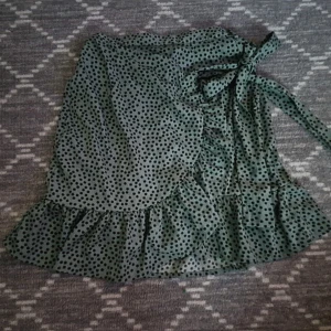 Grön blommig omlott kjol  - Omlott kjol med knytning och volanger. Fin grön färg med små blommor. Resår i midjan