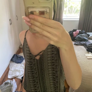 Svart och vit mönstrad linnetopp - Säljer en svart och vit linnetopp med tunna axelband och snyggt grafiskt mönster. Toppen har v-ringning framtill med knytdetalj och djup v-ringning i ryggen. Perfekt för varma dagar och enkel att styla med jeans eller shorts.