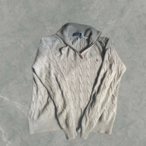 Grå kabelstickad halfzip från Polo Ralph Lauren - Säljer en snygg grå kabelstickad half zip från Ralph Lauren med dragkedja och klassiskt kabelstickat mönster. Tröjan har en liten blå broderad logga på bröstet och ribbade muddar. Perfekt för kyliga dagar! Den är i storlek S och i fint skick. Vid några frågor eller funderingar är det bara att höra av sig.