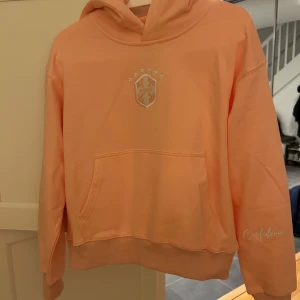 Avenir pink hoodie storlek XS - Superfin, rosa hoodie från Avenir med broderad logga och stjärnor på bröstet, texten 'Confidence' på ärmen och brodyr på huvan. Klassisk ficka på magen och ribbade muddar. Skön och avslappnad passform. Tröjan är helt ny och oanvänd. Nypris 1150kr