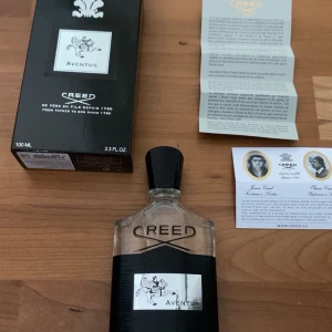 Creed Aventus 100ml parfym - Exklusiv Creed Aventus parfym på 100ml. Flaskan är genomskinlig med svart etikett och silverdetaljer, samt svart kork. Märkets logga och Aventus-motiv syns tydligt på framsidan. Levereras med originalkartong och medföljande papper.