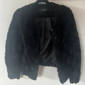 Svart pälsjacka från Vero Moda XS - Fluffig svart pälsjacka från Vero Moda i storlek XS. Jackan har långärmad design och är helsvart med mjuk fuskpäls som ger en lyxig känsla. Perfekt för dig som vill sticka ut med en trendig look under kyliga dagar.