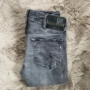 Replay grå slim fit jeans - Snygga grå jeans från Replay med slitna detaljer och coola bakfickor med broderad design. Modellen är slim fit och har klassisk femficksdesign. Jeansen är i stretchigt denim för extra komfort och har Replay-logga på insidan.