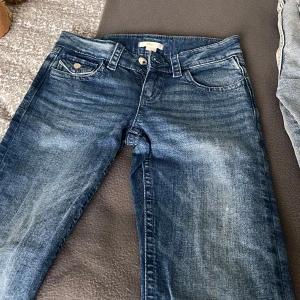 Blå jeans med broderad bakficka - Snygga blå jeans med slitningar och coolt broderi på bakfickan. Klassisk femficksmodell med knapp och dragkedja framtill. Jeansen har en rak passform och är perfekta för en avslappnad stil.
