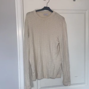 Beige kabelstickad tröja Selected Homme - Kabelstickad beige tröja från Selected Homme med rund halsringning och lång ärm. Tröjan har klassiskt flätmönster och är tillverkad i mjukt material som passar perfekt för kyligare dagar.