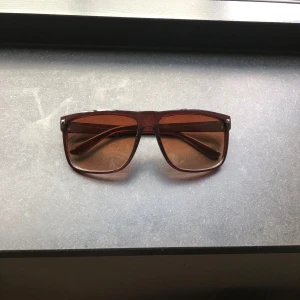 Bruna rayban-boyfriend liknande solglasögon - Snygga solglasögon med brun transparent båge och matchande bruna glas. Rektangulär form med breda skalmar ger en cool retrovibe. Perfekta för dig som vill sticka ut med en klassisk look. Lätta och bekväma att bära hela dagen.