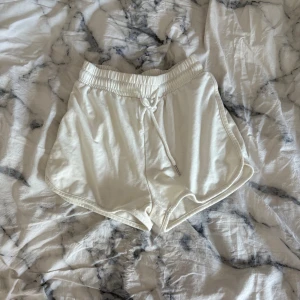 Vita shorts med snörning - Snygga vita shorts med elastisk midja och snörning framtill. De har en sportig look med rundade kanter och är tillverkade i mjuk bomull, perfekta för varma dagar. Passformen är loose och de är superbekväma att ha på sig.