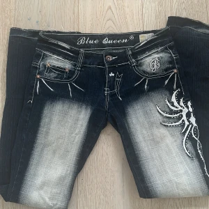 Blue Queen jeans med broderi - Mörkblå jeans från Blue Queen med kraftig blekning och vit kontrastsöm. Snyggt broderi och nitar på ena benet samt dekorativa detaljer vid fickorna. Jeansen har låg midja och en rak passform 