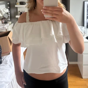 Vit offshoulder volangblus Gina Tricot - Supersöt vit blus från Gina Tricot med offshoulder-modell och dubbla volanger upptill. Luftig och lätt i materialet, perfekt för varma dagar. Sitter snyggt och ger en romantisk vibe till din outfit. Helt oanvänd med prislappen kvar