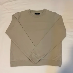 Sweatshirt - En stilren beige crewneck med rund halsringning och ribbad med muddar vid ärmslut och nederkant. Tröjan är enkel och clean utan tryck eller mönster, perfekt för en chill och avslappnad look. Tillverkad i mjuk bomull för skön komfort.