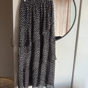 Svartvit volangkjol med prickigt mönster - Säljer en svart kjol med vita prickar och flera volanger. Kjolen har resår i midjan och är i ett lätt, luftigt material som ger en flowy känsla. Perfekt för dig som gillar en lekfull och trendig stil.