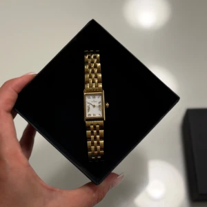 Guldig rektangulär klocka Mockberg - Säljer en vacker Mockberg klocka med en elegant guldfärgad design. Klockan har en rektangulär urtavla med romerska siffror, vilket ger den en klassisk touch. Extra länkbitar och originalförpackning medföljer. Knappt använd. Behöver batteribyte. 
