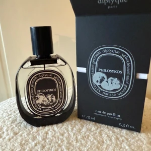 Diptyque Philosykos Eau de Parfum 75ml - Diptyque Philosykos Eau de Parfum i en elegant oval glasflaska med svart lock och svartvit etikett. Flaskan rymmer 75 ml och har en stilren design med konstnärlig illustration. Kommer med originalförpackning i svart kartong. Kan även bytas!