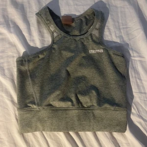 Grå träningstopp från Stronger - Sportig grå linnetopp från Stronger med brottarrygg och meshdetaljer vid axlarna. Toppen har en tight passform och är tillverkad i ett stretchigt syntetmaterial som andas, perfekt för träning och aktiva dagar. Använd ett flertal gånger men inga defekter.