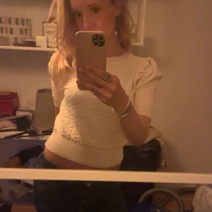 Krämvit croppad topp med puffärm - Superfin krämvit croppad topp med korta puffärmar och strukturmönster på framsidan. Tight passform och bred mudd nedtill ger en snygg siluett. Perfekt att styla med jeans eller kjol för en trendig look. Vet tyvärr inte var den är ifrån