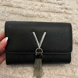 Svart axelväska med silverdetaljer från Valentino - Snygg svart axelväska från Valentino i skinnimitation med silverfärgad kedja och V-logga framtill. Väskan har dekorativa silverfransar och praktiska fack inuti. Inget kvitto kvar. Nästan aldrig använd och i väldigt fint skick! Vet ej om den är 100% äkta 