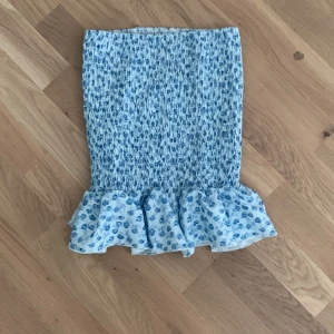 Blommig blå volangkjol från SHEIN - Supersöt kort kjol från SHEIN i ljusblått med små blå blommor och volangkant nedtill. Kjolen är smockad och har en tight passform som framhäver midjan. Perfekt för dig som gillar en feminin och trendig stil.