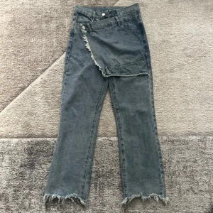 Grå jeans med fransade detaljer - Unika grå jeans i rak modell med cool omlott-detalj framtill och fransade benslut. Jeansen har klassiska fickor och bälteshällor, och är tillverkade i ett robust denimtyg. Perfekta för dig som vill sticka ut med en edgy streetstyle. står storlek M men skulle säga att de är mer some storlek S eller XS eftersom det är asiatisk storlek