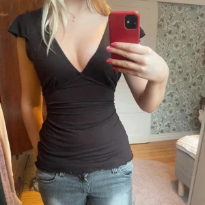 Brun omlottopp med knyt i midjan - Säljer en brun omlottopp med djup v-ringning och knyt i midjan. Toppen har korta ärmar och smickrande passform som framhäver midjan. Perfekt att styla med jeans eller kjol för en trendig look.