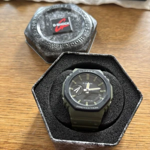 Grön G-Shock klocka med digital display - Säljer en grön G-Shock klocka med robust design och digital display. Klockan har svart urtavla, tydliga index och flera funktioner som timer och ljus. Armbandet är i tålig syntet och spännet är i silverfärgad metall. Perfekt för dig som gillar en sportig och cool stil.