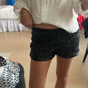 Svarta paljettshorts från Stradivarius - Glittriga svarta shorts från Stradivarius, täckta med paljetter för en riktigt festlig look. De har en elastisk midja och är fodrade med mjukt tyg på insidan. 